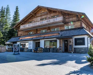Traditionelles Holzgebäude mit Balkonen und einer einladenden Außenterrasse, umgeben von Bäumen.
