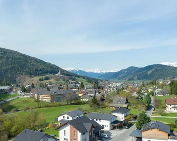 Panoramablick auf eine malerische Berglandschaft mit Siedlung und grünen Hügeln.