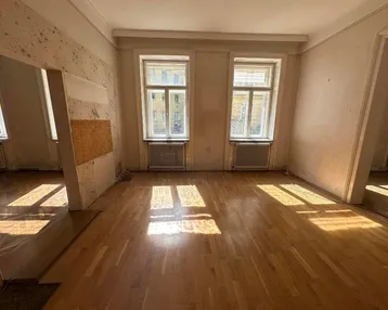 Helles Zimmer mit Holzboden und zwei Fenstern, bereit für Renovierung.