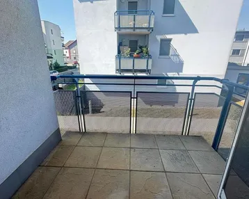 Heller Balkon mit Fliesenboden und Metallgeländer, bietet einen Blick auf die umliegenden Gebäude.