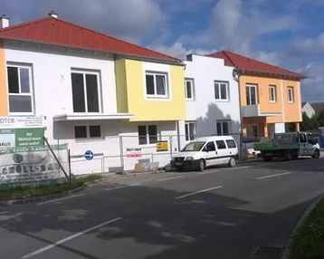Neue Wohngebäude mit farbigen Fassaden und roten Dächern entlang einer Straße, teilweise noch im Bau.
