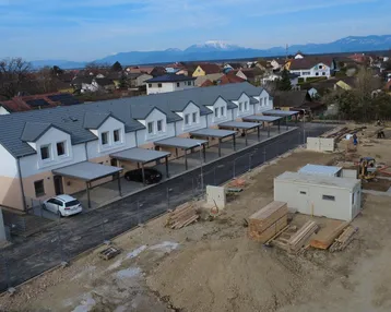 Luftaufnahme einer Reihe von Neubauhäusern mit Carports und einer Baustelle im Vordergrund.