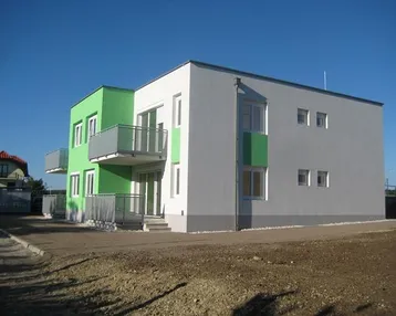 Modernes Mehrfamilienhaus mit grünen und grauen Fassaden, Balkonen und Flachdach in einem Neubaugebiet.