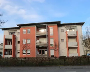 Modernes Mehrfamilienhaus mit orangefarbener Fassade, Balkonen und Rollläden in einer Wohngegend.
