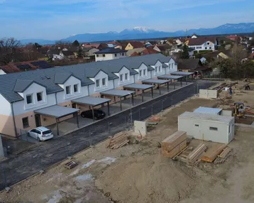 Luftaufnahme einer Reihe von Neubau-Reihenhäusern mit Carports und angrenzender Baustelle.