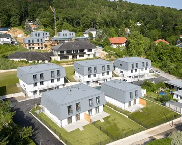 Luftaufnahme einer modernen Wohnsiedlung mit mehreren Häusern und grüner Umgebung am Waldrand.