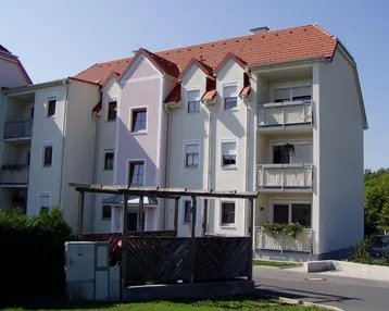 Mehrstöckiges Wohngebäude mit hellen Fassaden, roten Ziegeldächern und mehreren Balkonen.