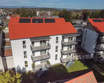Luftaufnahme von modernen Wohngebäuden mit roten Dächern und Solaranlagen in grüner Umgebung.