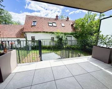 Geräumige Terrasse mit Fliesenboden und Blick auf ein charmantes Altbaugebäude mit Garten.