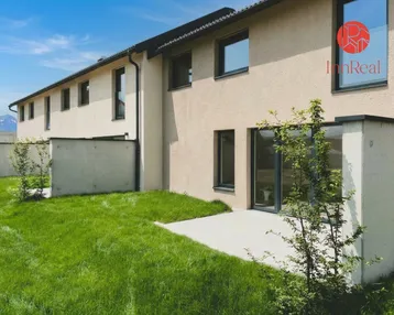 Moderne Reihenhäuser mit gepflegtem Garten, Terrasse und Bergblick unter blauem Himmel.