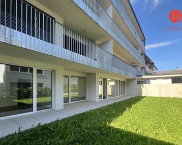 Moderne Wohnanlage mit Balkonen und Grünfläche im Erdgeschoss.