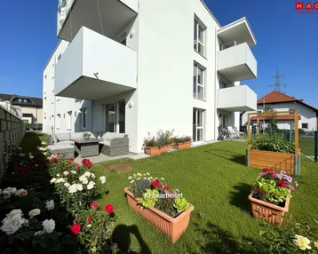 Moderner Neubau mit Balkonen und einer gepflegten Gartenanlage inklusive Sitzbereich und Blumenbeeten.