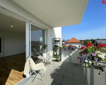 Heller Balkon mit Fliesenboden, Gartenmöbeln und bunten Blumenkästen, ideal zum Entspannen im Freien.