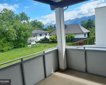 Geräumiger Balkon mit Blick auf grüne Wiesen und die umliegende Berglandschaft unter blauem Himmel.