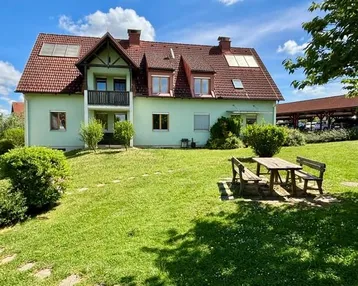 Gepflegtes Einfamilienhaus mit hellgrüner Fassade, Satteldach, Balkon und großem Garten mit Sitzbereich.