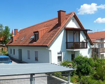 Gepflegtes Einfamilienhaus mit rotem Ziegeldach, weißer Fassade und kleinem Balkon.