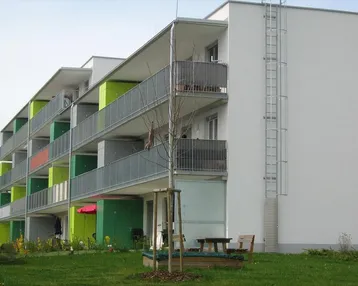 Modernes Mehrfamilienhaus mit farbigen Balkonen und gepflegter Grünfläche im Vordergrund.