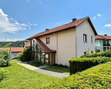 Einfamilienhaus mit Garten und verglastem Eingangsbereich unter blauem Himmel.