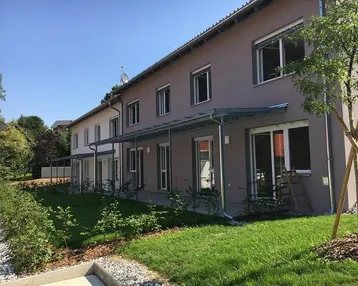 Moderne Reihenhäuser mit gepflegten Vorgärten und überdachten Terrassen unter blauem Himmel.