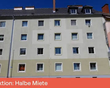 Mehrstöckiges Wohngebäude mit beigefarbener Fassade, Mansarddach und Dachgauben unter blauem Himmel.