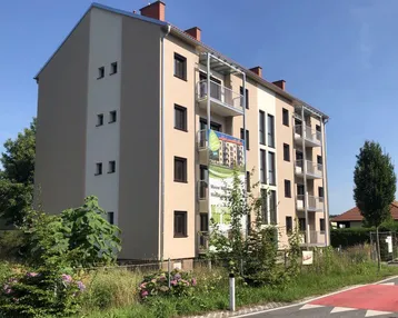 Modernes Mehrfamilienhaus mit beiger Fassade, Balkonen und umgebender Grünfläche.