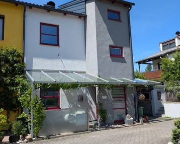 Modernes Reihenhaus mit heller Fassade, roten Fensterrahmen und überdachtem Eingangsbereich.