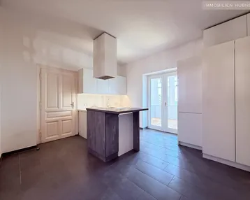 Moderne Küche mit weißen Schränken, dunkler Kücheninsel und Zugang zu einem Außenbereich.