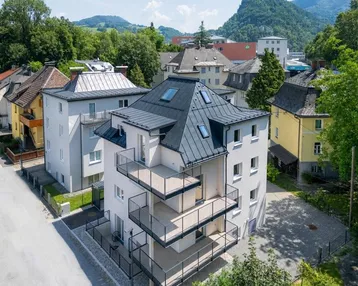 Modernes Mehrfamilienhaus mit mehreren Balkonen und Blick auf die umliegende Berglandschaft.