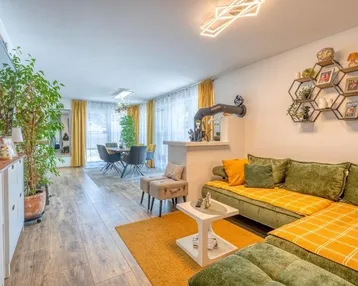Gemütlicher Wohn-Essbereich mit grünem Sofa, Holzboden und farbenfroher Dekoration.