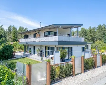 Modernes Einfamilienhaus mit mehreren Balkonen, Garten und umzäuntem Grundstück.