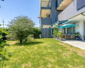 Gepflegter Gartenbereich mit Rasenfläche und angrenzender Terrasse eines modernen Wohngebäudes.