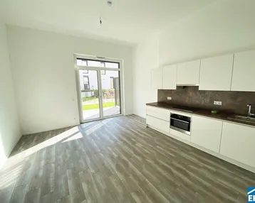 Heller offener Wohnbereich mit integrierter Küche, Holzboden und Zugang zum Garten.