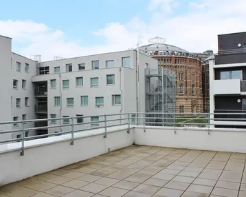 Geräumige Terrasse mit Fliesenboden und Blick auf moderne Gebäude sowie historische Architektur.