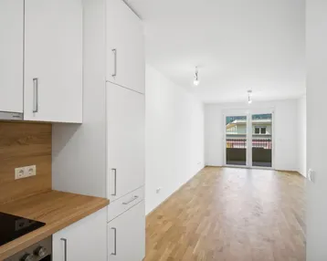 Helle, offene Wohnküche mit modernem Parkettboden und Zugang zu einem Balkon mit Bergblick.