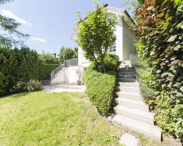 Großzügiger Gartenbereich mit Rasenfläche und Treppenaufgang zum Haus, umgeben von Hecken.