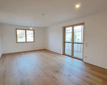 Helles Zimmer mit Holzboden und Zugang zu einem Balkon, ideal als Wohnbereich.