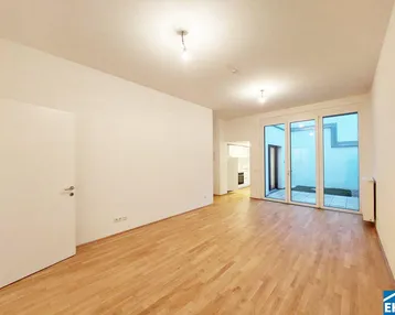 Geräumiges Wohnzimmer mit hellem Parkettboden und Zugang zu einem kleinen Außenbereich durch große Glastüren.