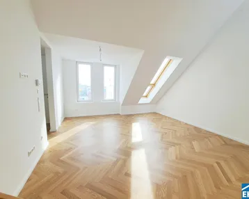 Lichtdurchfluteter Raum mit schrägem Dachfenster und hellem Fischgrätparkettboden.