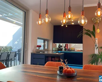 Moderner Essbereich mit Holztisch, orangefarbenen Stühlen und offener Küche, mit Zugang zur Terrasse.