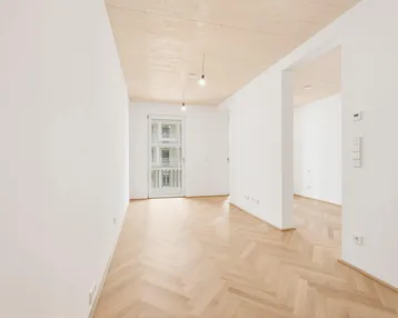 Helles, unmöbliertes Zimmer mit Fischgrätparkett und Zugang zu einem französischen Balkon.