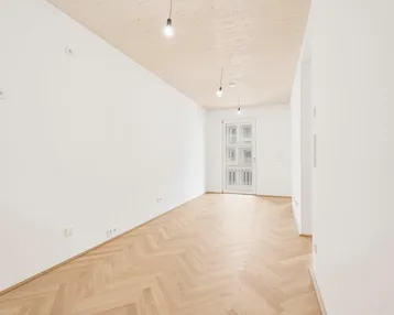 Heller, leerer Raum mit Fischgrätparkett, weißen Wänden und Holzbalkendecke, bereit zur individuellen Gestaltung.