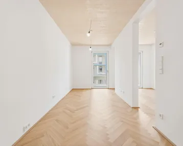 Heller, leerer Raum mit Fischgrätparkett, weißen Wänden und Zugang zu einem Balkon.