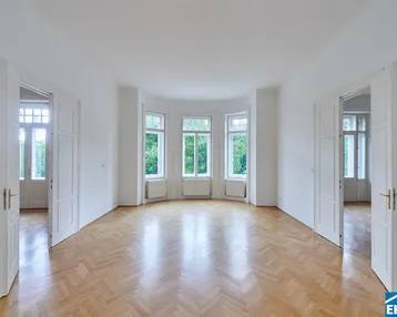 Großzügiges Wohnzimmer mit hellem Fischgrätparkett und mehreren Türen.