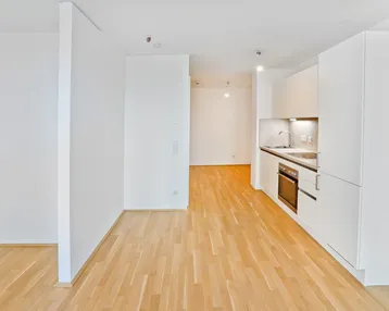 Helles Wohnzimmer mit integrierter Küchenzeile und Parkettboden, offen gestaltet.