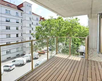 Geräumiger Balkon mit Holzfußboden und Glasgeländer, bietet Blick auf die umliegenden Gebäude und Bäume.