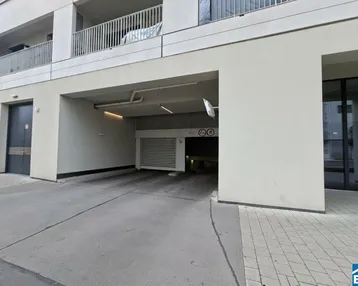 Einfahrt zur Tiefgarage eines modernen Wohngebäudes mit klaren Linien und Balkonen im Hintergrund.