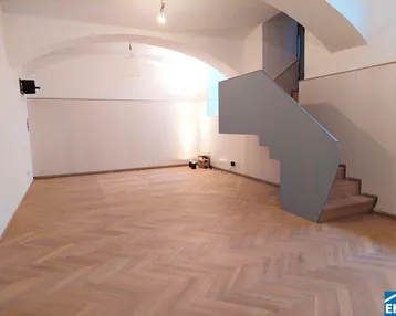 Geräumiger Innenraum mit elegantem Fischgrätparkett, gewölbten Decken und einer modernen Treppe.