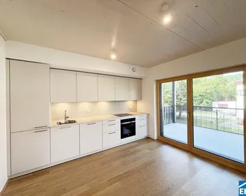 Moderne Einbauküche in einem offenen Wohnbereich mit Zugang zum Balkon und Holzboden.