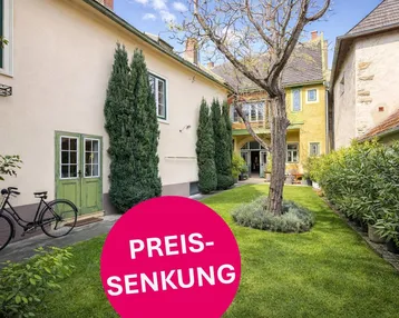 Gepflegter Gartenbereich mit Rasenfläche, einem alten Baum und einer Reihe von Zypressen entlang der Hauswand.