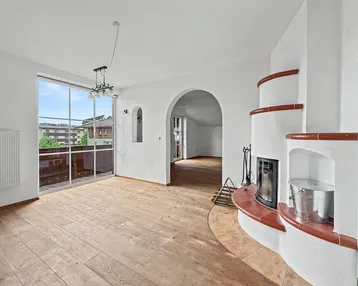 Geräumiges Wohnzimmer mit Holzboden, Kamin und Zugang zu einem Balkon mit Ausblick.